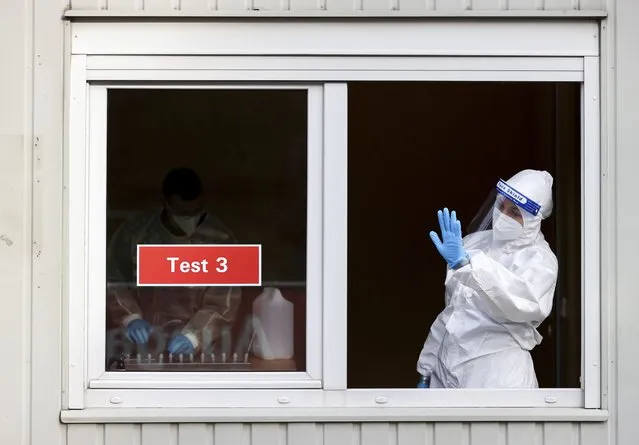 A woman in protective clothing beckons test takers to her window at a test center with the start of the model project in ugustusburg, Germany, Thursday, April 1, 2021. After five months of lockdown, hotels and restaurants here have reopened to private visitors. (Photo by Jan Woitas/dpa via AP Photo)