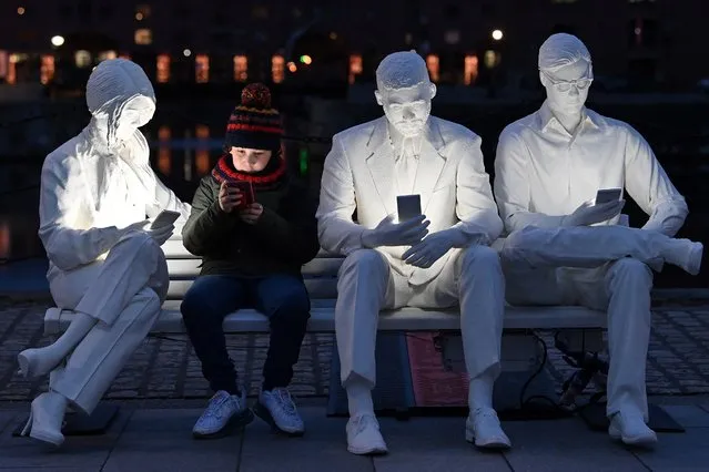 A boy poses with a mobile phone whilst sitting on the installation “Absorbed by Light”, by artist Gali May Lucas, during a preview for the “River of Light” Trail in Liverpool, northwest England on March 22, 2021. 11 audio and visual installations will form the two kilometre “River of Light” Trail, which opens to the public on March 23. (Photo by Paul Ellis/AFP Photo)