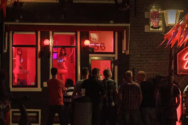 Netherlands, North Holland, Amsterdam, Oudezijds Achterburgwal canal, De Wallen, also called Red Light District in English, group of men watching prostitutes posing behind the window of their one-room cabin. (Photo by Alamy Stock Photo)