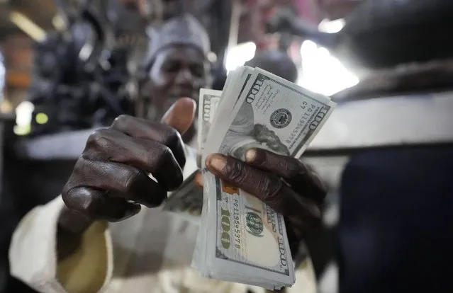 A man counts U.S. $100 bills at the craft and art market in Lagos, Nigeria, on Wednesday, August 16, 2023. Across the developing world, many countries are fed up with America's dominance of the global financial system – and especially the power of the dollar. (Photo by Sunday Alamba/AP Photo)