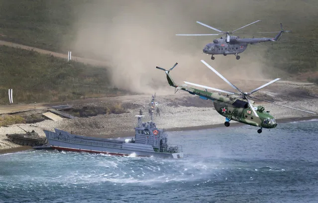 A Russian navy landing vessel unloads an armored vehicle as military helicopters fly overhead during Russian military maneuvers Vostok 2018 on the training ground “Klerk”, about 50 kilometers (31 miles) south of Vladivostok, Russian Far East port, Russia, Saturday, September 15, 2018. The weeklong Vostok 2018 maneuvers are the largest war games Russia ever had. (Photo by Sergei Grits/AP Photo)
