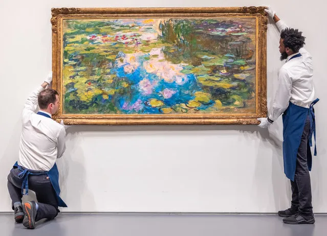 An undated handout photo made available by the auction house Sotheby's shows two employees hanging the work “Le Bassin aux nympheas”, by the French painter Claude Monet, painted between 1917 and 1919 and considered as “one of the most exceptional paintings by Monet that has hit the market in recent history.”, in New York, USA (issued 13 May 2021). The painting of the famous series of water lilies by Claude Monet was the star of the night at a Sotheby's auction held this Wednesday in New York, where it fetched 70.3 million dollars, substantially exceeding the expectations of experts. (Photo by Sotheby's/EPA/EFE)