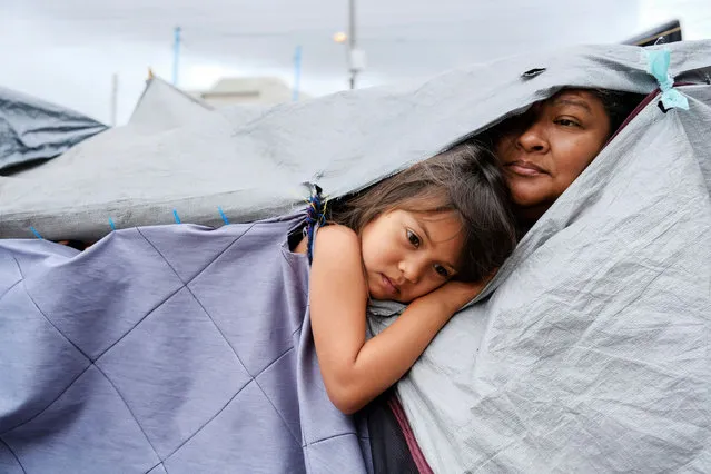 Honduran migrants Kami, 5, and her aunt Mariana listen as other migrants discuss hygiene norms within the migrant camp, at a makeshift camp at the El Chaparral border port of entry with the U.S., in Tijuana, Mexico on April 22, 2021. (Photo by Toya Sarno Jordan/Reuters)