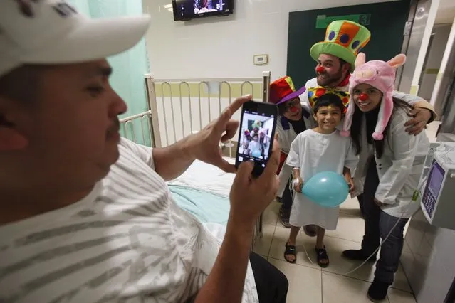 A man takes a picture of his son with members of “Laughter Doctors of Ciudad Juarez” at a children's hospital in Ciudad Juarez March 11, 2015. (Photo by Jose Luis Gonzalez/Reuters)