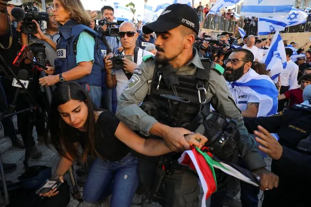 An Israeli policeman tries to take a Palestinian flag from a woman as youth from far-right Israeli groups participate in a flag-waving procession at Damascus Gate, just outside Jerusalem's Old City on June 15, 2021. (Photo by Ammar Awad/Reuters)