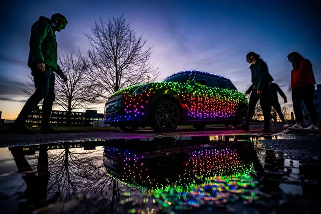 People walk past an illuminated Mini car at the Mini Plant in Oxford on Thursday, November 17, 2022. The driver of a Mini decorated in 3,000 twinkling lights hopes to “bring little moments of joy to people's lives” this Christmas and raise over £10,000 for charity. (Photo by Ben Birchall/PA Images via Getty Images)