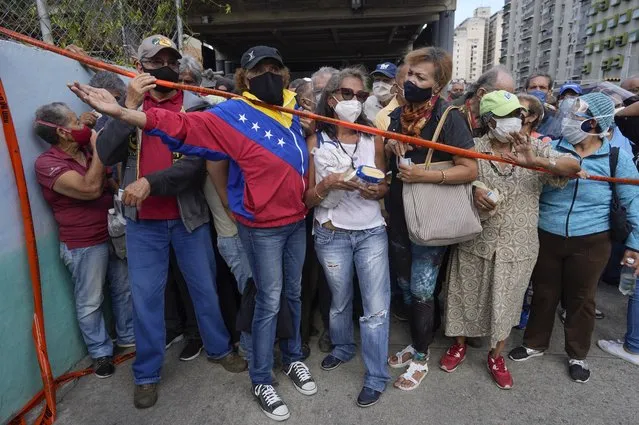Residents stand behind a strip of tape serving as a barrier as they gather outside a vaccination center looking to be inoculated with a second dose of the Sputnik V COVID-19 vaccine, in Caracas, Venezuela, Thursday, September 16, 2021. The Venezuelan government is beginning rollouts of second doses following months of delays. (Photo by Ariana Cubillos/AP Photo)