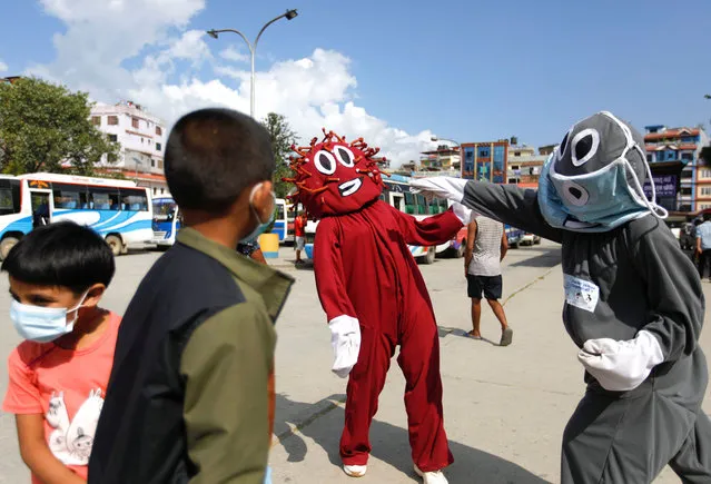 Anisha Prajapati, in a mask costume, playfully takes a swing at Sajani Shrestha, in a coronavirus-themed disguise, in front of a group of kids at a bus station, to spread awareness of mask-wearing, amid the COVID-19 pandemic, as people head to their villages for Dashain, the biggest religious festival for Hindus in Nepal, in Kathmandu, Nepal October 7, 2021. (Photo by Navesh Chitrakar/Reuters)