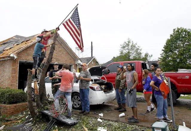 Aldyn Roan and David Arce (top) mount an American flag to a broken tree trunk in front of the Arce home after a tornado swept through the area the previous night in Van, Texas May 11, 2015. (Photo by Mike Stone/Reuters)
