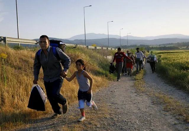 Kurdish Syrian immigrant Sahin Serko holds his 7 year-old daughter Ariana as they run to hide from patrolling Greek police before crossing the border along with another 45 Syrian immigrants into Macedonia near the Greek village of Idomeni in Kilkis prefecture May 14, 2015. (Photo by Yannis Behrakis/Reuters)