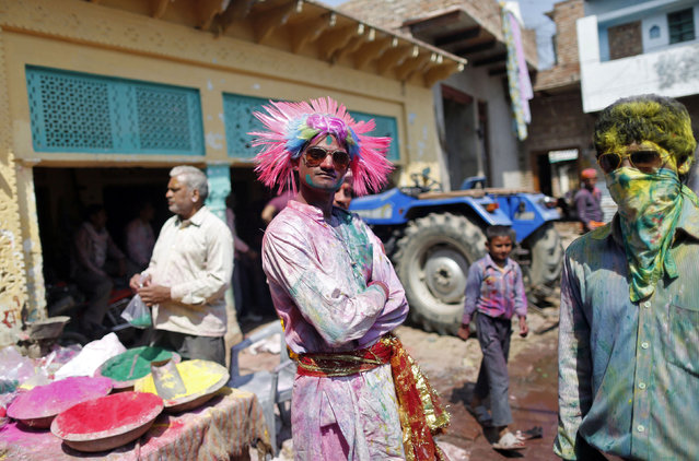A Hindu devotee with his face daubed in colours reacts to the camera while taking part during “Lathmar Holi” at the village of Barsana in the northern Indian state of Uttar Pradesh March 9, 2014. In a Holi tradition unique to Barsana and Nandgaon villages, men sing provocative songs to gain the attention of women, who then “beat” them with bamboo sticks called “lathis”. Holi, also known as the Festival of Colours, heralds the beginning of spring and is celebrated all over India. (Photo by Anindito Mukherjee/Reuters)