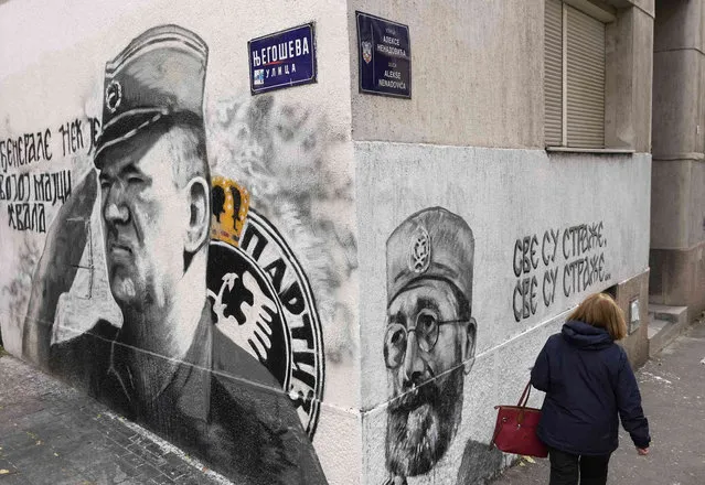 A woman walks by a mural of former Bosnian Serb military chief Ratko Mladic, left, and newly draw mural of controversial Serb World War II leader Gen. Dragoljub Draza Mihailovic in Belgrade, Serbia, Wednesday, November 17, 2021. (Photo by Darko Vojinovic/AP Photo)