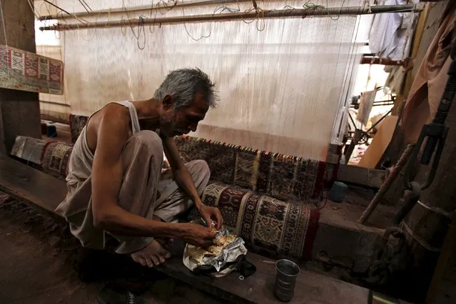 A traditional carpet weaver eats lunch as he takes a break from work on a carpet on a handmade loom in a workshop on the outskirts of Karachi, Pakistan April 11, 2016. (Photo by Akhtar Soomro/Reuters)