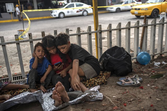 The Bolaños children, from left, Sebastian, Kamila and Miguel Angel, from Venezuela, watch videos on a mobile phone outside the bus terminal where they are living with their single mother Keilly and one other sibling, along with other migrants in Villahermosa, Mexico, Saturday, June 8, 2024. Their mother was captured in the northern state of Juarez, where she said she was beaten by the military in front of her children, loaded on a bus for two days, and left in Villahermosa. (Photo by Felix Marquez/AP Photo)