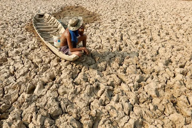 A fisherman sits to smoke on his boat at a Bak Angrout dried up pond at the drought-hit Kandal province in Cambodia May 13, 2016. (Photo by Samrang Pring/Reuters)