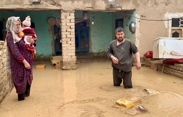 An Afghan woman holds her child as a man salvages his belongings from flood waters outside their house in Maymana, the capital city of Faryab Province, Afghanistan, on May 19, 2024. (Photo by Reuters/Stringer)