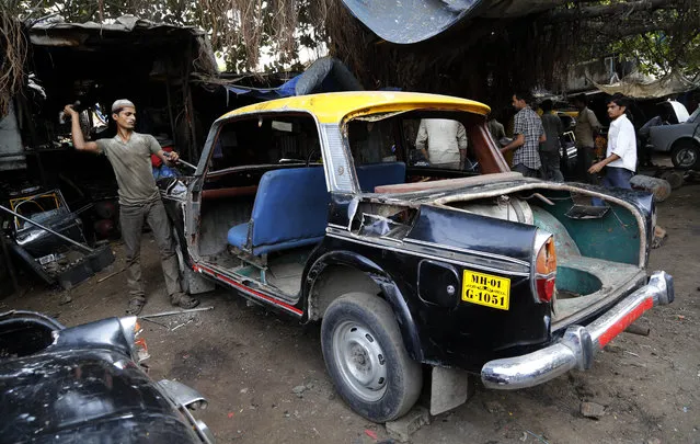 In this Wednesday, March 26, 2014 photo, a worker dismantles a taxi at a junk yard in Mumbai, India. The distinctive black-and-yellow licensed cabs number just 42,000 in Mumbai, inadequate for a city of 22 million. Taxi-hailing smartphone app Uber is making a big push into Asia with the company starting operations in 18 cities in Asia and the South Pacific including Seoul, Shanghai, Bangkok, Hong Kong and five Indian cities in the last year. (Photo by Rajanish Kakade/AP Photo)