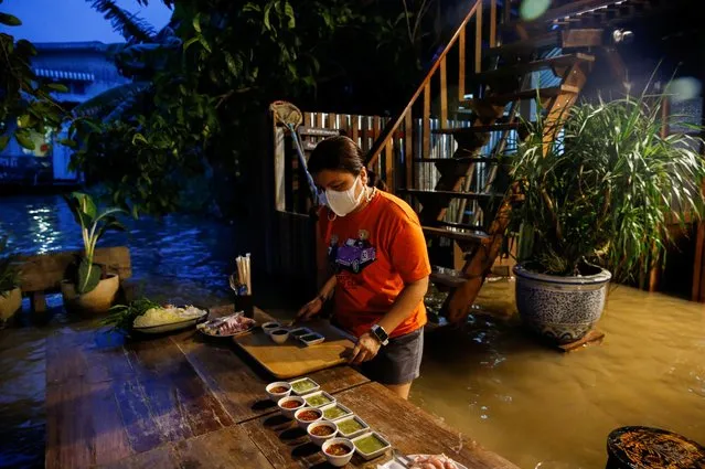 A staff member prepares food for customers at a flooded restaurant, where patrons stand up from their tables every time the waves comes in, on a river bank in Nonthaburi near Bangkok, Thailand, October 7, 2021. Videos have gone viral on social media of customers sitting on drenched chairs, taking mouthfuls of food as long-tail boats buzz by, then moving out of the way as waves hit. (Photo by Soe Zeya Tun/Reuters)