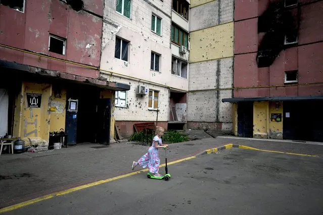 A girl rides a scooter near destroyed buildings during attacks in Irpin outskirts Kyiv, Ukraine, Thursday, June 2, 2022. (Photo by Natacha Pisarenko/AP Photo)