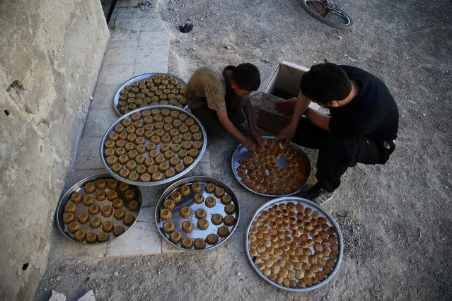 A man and a boy arrange traditional sweets in a tray ahead of the Eid al-Fitr holiday marking the end of Ramadan in the rebel held besieged town of Douma, eastern Ghouta in Damascus, Syria July 3, 2016. (Photo by Bassam Khabieh/Reuters)