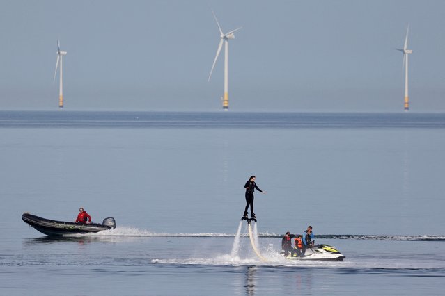 A speedboat passes a person using a flyboard near a wind farm on an unseasonably hot day in Herne Bay, Britain on October 8, 2023. (Photo by Kevin Coombs/Reuters)