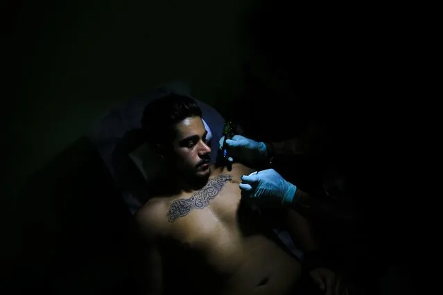 In this Wednesday, July 20, 2016 photo, tattoo artist Hussein Al-Hussein inks the chest of client Alodi Issa, 22, with Shiite Muslim religious slogans at his tattoo shop in the southern suburb of Beirut, Lebanon. The tattoo in Arabic reads, “Oh, the revenge for Hussein. Ali, Fatima”