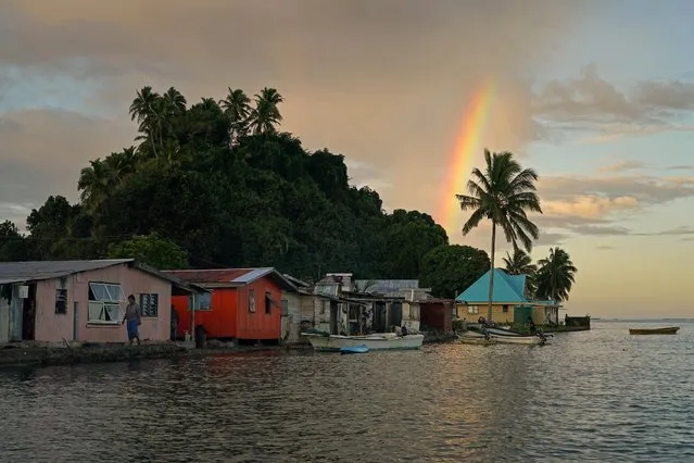 Local resident Tarusila Boseiwaqa walks along a sea wall that no longer protects homes from the intrusion of water at higher tides, as a rainbow forms over Serua Village, Fiji on July 14, 2022. As the community runs out of ways to adapt to the rising Pacific Ocean, the 80 villagers face the painful decision whether to move. (Photo by Loren Elliott/Reuters)