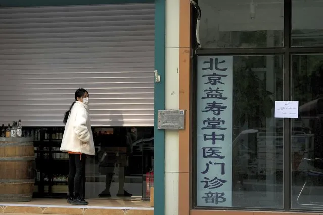 A woman wearing a face mask closes her liquor store along with a shuttered traditional medicine clinic which is located near a neighborhood locked down area for health monitoring following a COVID-19 case detected in Beijing, Wednesday, November 9, 2022. (Photo by Andy Wong/AP Photo)