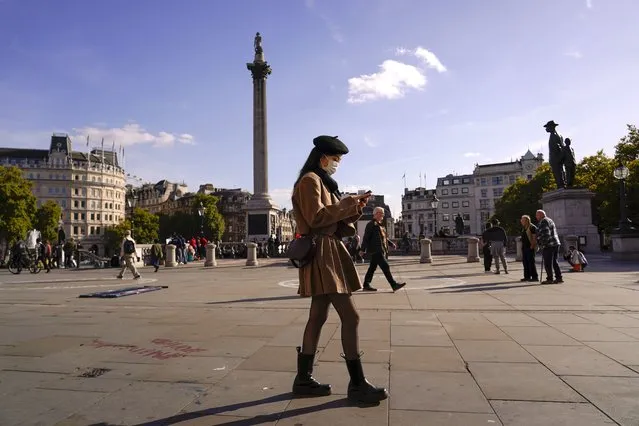 A woman wears a face mask as she walks in Trafalgar Square, in London, Tuesday, October 11, 2022. (Photo by Alberto Pezzali/AP Photo)