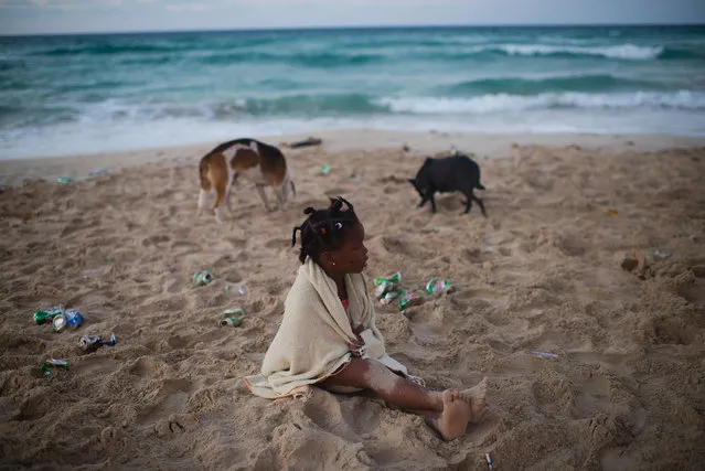 Four-year-old Estefany Gloria Garcia sits on the littered shore of Santa Maria beach, which is about 15 miles from Havana. Her mother was partying with her friends. It is the closest beach to Havana. The government is demolishing buildings all over the coast of East Havana and recovering and restoring beach dunes. (Photo by Sarah L. Voisin/The Washington Post)