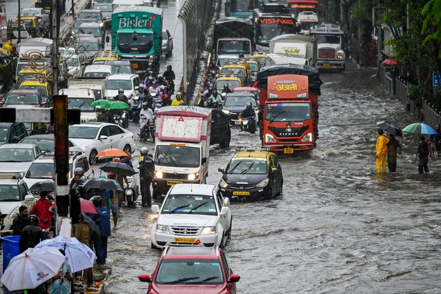 Commuters lie stuck in traffic as they wade through a flooded street after heavy rain showers in Mumbai on May 26, 2025. Lashing rains swamped India's financial capital Mumbai on May 26 as the annual monsoon arrived some two weeks earlier than usual, according to weather forecasters. (Photo by Punit Paranjpe/AFP Photo)