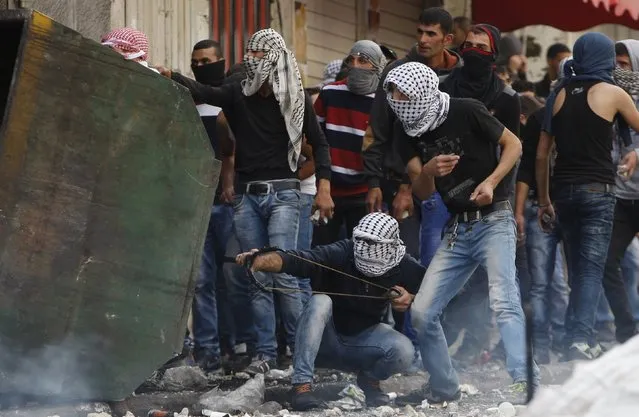 A masked Palestinian protester uses a slingshot to throw stones at Israeli troops as others take cover during clashes in the West Bank city of Hebron October 9, 2015. (Photo by Mussa Qawasma/Reuters)