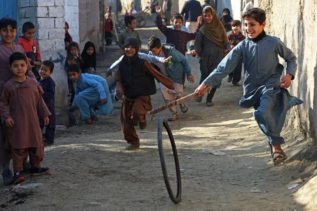 Afghan children play with a tyre along a street in Jalalabad on January 9, 2023. (Photo by AFP Photo/Stringer)