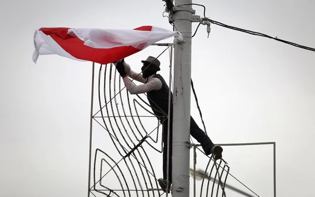 A man in a mask hangs an old Belarusian flag on a light pole during an opposition rally to protest the official presidential election results in Minsk, Belarus, Sunday, September 27, 2020. (Photo by TUT.by via AP Photo)