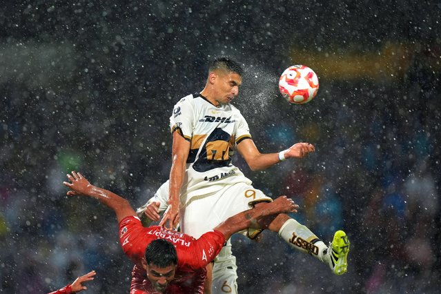 Rain pours down as Pumas' Guillermo Martínez heads the ball over Necaxa's Tomas Badaloni during a Mexican soccer league match in Mexico City, August 10, 2025. (Photo by Fernando Llano/AP Photo)