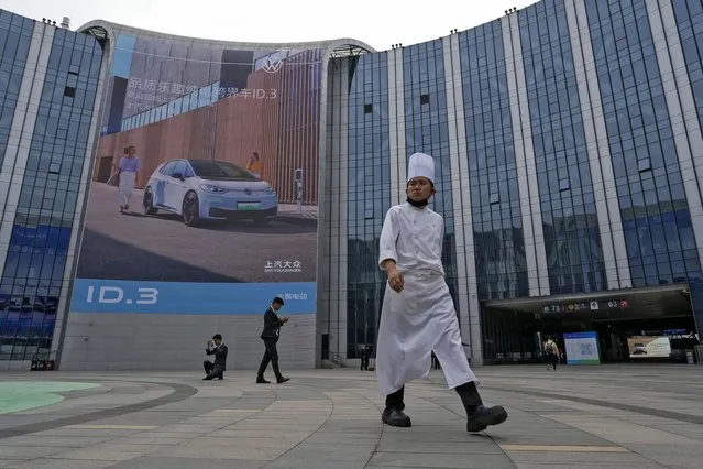A chef and workers hang out near an advertisement for Volkswagen ID.3 on display at the National Exhibition and Convention Center during the Auto Shanghai 2023 in Shanghai, China, Tuesday, April 18, 2023. (Photo by Ng Han Guan/AP Photo)