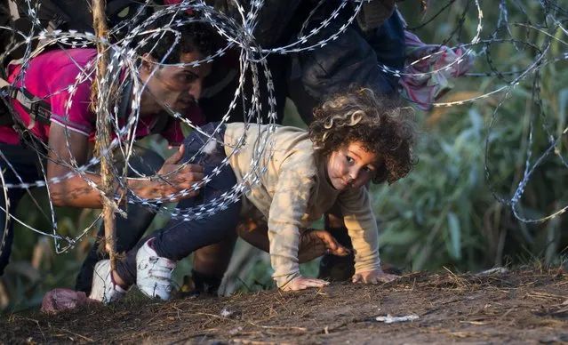 In this Thursday, Aug. 27, 2015 file photo, a child is helped cross from Serbia to Hungary through the barbed wire fence near Roszke, southern Hungary. The Hungarian government has submitted to parliament Constitutional amendments and a new draft law further tightening the country’s laws on refugees and asylum-seekers. The legislation submitted Tuesday, which complements draft bills presented earlier this year by Prime Minister Viktor Orban’s Cabinet, seeks to prevent Hungary “from becoming an immigrant country”. (Photo by Darko Bandic/AP Photo)