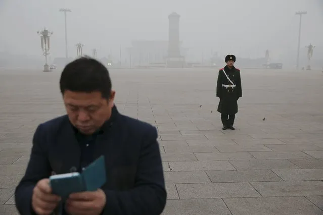 A man checks his phone in front of a paramilitary soldier at the Tiananmen Square on an extremely polluted day as hazardous, choking smog continues to blanket Beijing, China December 1, 2015. (Photo by Damir Sagolj/Reuters)