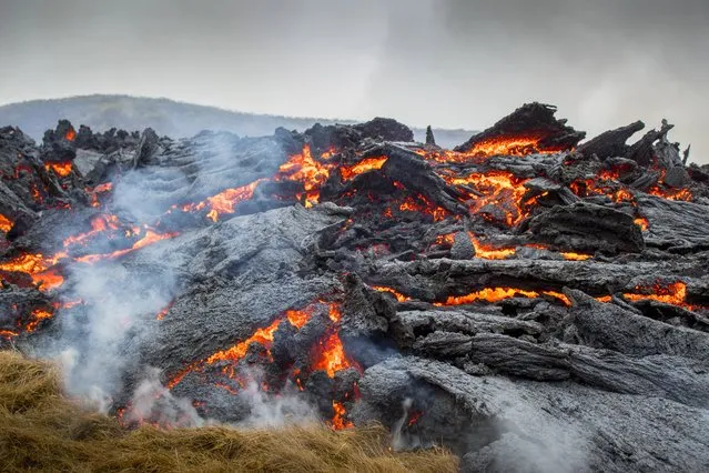 Lava flows from the erupting Fagradalsfjall volcano some 40 km west of the Icelandic capital Reykjavik, on March 21, 2021. Weekend hikers took the opportunity Sunday to inspect the area where a volcano erupted in Iceland on March 19, some 40 kilometres (25 miles) from the capital Reykjavik, the Icelandic Meteorological Office said, as a red cloud lit up the night sky and a no-fly zone was established in the area. (Photo by Marco Di Marco/AP Photo)