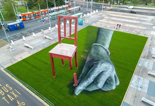 A land art painting called  “ALL OF US!” meant to draw attention to the plight of civilians in armed conflicts and made by Swiss French artist SAYPE, dialogues with the Broken Chair, on the Place des Nations in front of the United Nations in Geneva, Switzerland on September 11, 2023. (Photo by Denis Balibouse/Reuters)