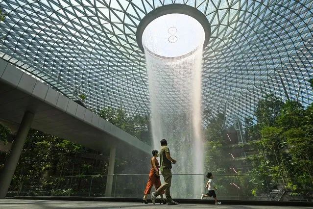 A family walks past the rain vortex at Jewel Changi Airport in Singapore on June 23, 2021. (Photo by Roslan Rahman/AFP Photo)