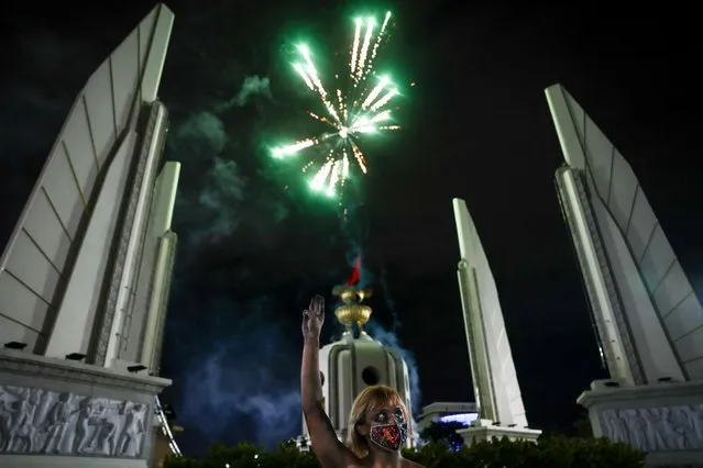 A protester flashes a three finger salute as fireworks explode over the Democracy Monument during a demonstration calling for the resignation of Thailand's Prime Minister Prayut Chan-O-Cha over the government's handling of the Covid-19 coronavirus crisis in Bangkok on August 28, 2021. (Photo by Jack Taylor/AFP Photo)