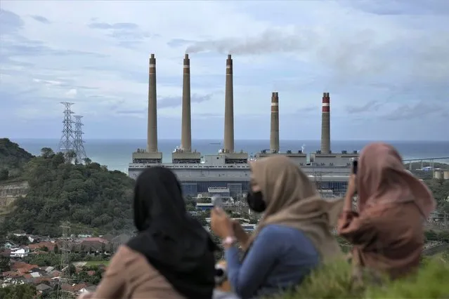 Indonesian women sit on a hill as the Suralaya coal power plant looms in the background in Cilegon, Indonesia, on January 8, 2023. A plan for how Indonesia will spend $20 billion to transition to cleaner energy was submitted Wednesday, Aug. 16, to the government and its financing partners, the planners said. (Photo by Dita Alangkara/AP Photo)