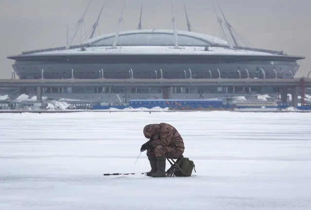 A man fishes through an ice hole in the Finnish Gulf in St. Petersburg, Russia, Wednesday, January 25, 2017, with the new soccer stadium on Krestovsky Island which will host some of Confederations Cup 2017 and World Cup 2018 soccer matches in the background. (Photo by Dmitri Lovetsky/AP Photo)