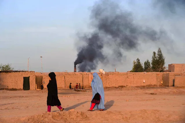 In this photograph taken on April 3, 2019, Afghan women walk near a brick factory as smoke rises up in the sky from a chimney on the outskirts of Jalalabad. (Photo by Noorullah Shirzada/AFP Photo)