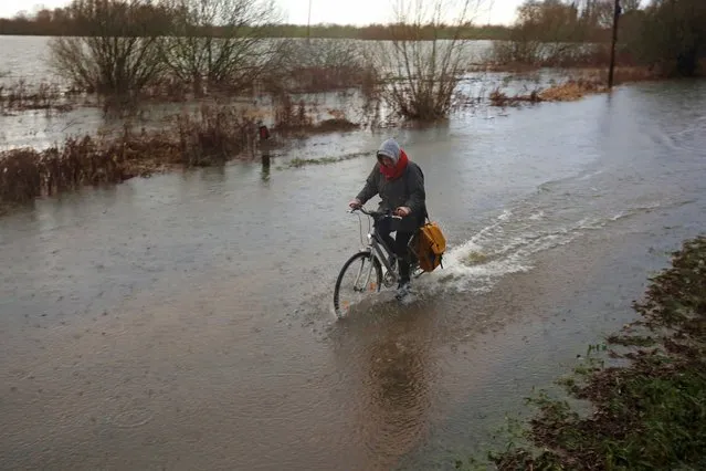 A person cycles through the flooded road at Sutton Gault in Cambridgeshire, England. The levels of the River Great Ouse at Sutton Gault have risen rapidly within the last 24 hours leading to floods in this area of Cambridge, on December 28, 2021. (Photo by Paul Marriott/Rex Features/Shutterstock)