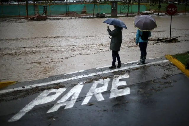 People stand next to a flooded street in Santiago, April 17, 2016. The sign on the ground reads “Stop”. (Photo by Ivan Alvarado/Reuters)