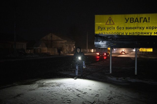 A woman walks with a torch in the village of Kolychivka, Ukraine, Wednesday, February 1, 2023. (Photo by Daniel Cole/AP Photo)
