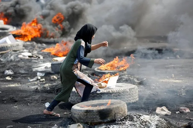 A demonstrator runs between burning tires during a curfew, two days after the nationwide anti-government protests turned violent, in Baghdad, Iraq on October 3, 2019. (Photo by Wissm al-Okili/Reuters)