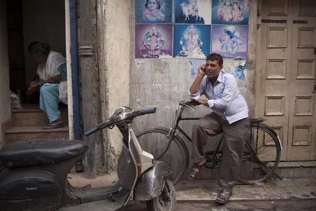 An Indian man speaks on his phone as he sits on a cycle parked in front of the portraits of Hindu gods and goddesses at a narrow alley in old quarters of Delhi, India, Saturday, July 25, 2015. Old Delhi despite of being extremely crowded and dilapidated still serves as the symbolic heart of the city. (Photo by Tsering Topgyal/AP Photo)